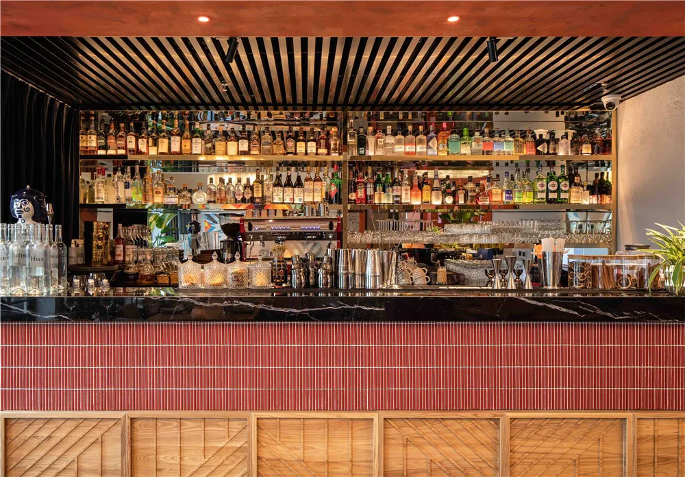 A sleek, modern bar counter featuring a marble top, with a variety of liquor bottles and glassware.