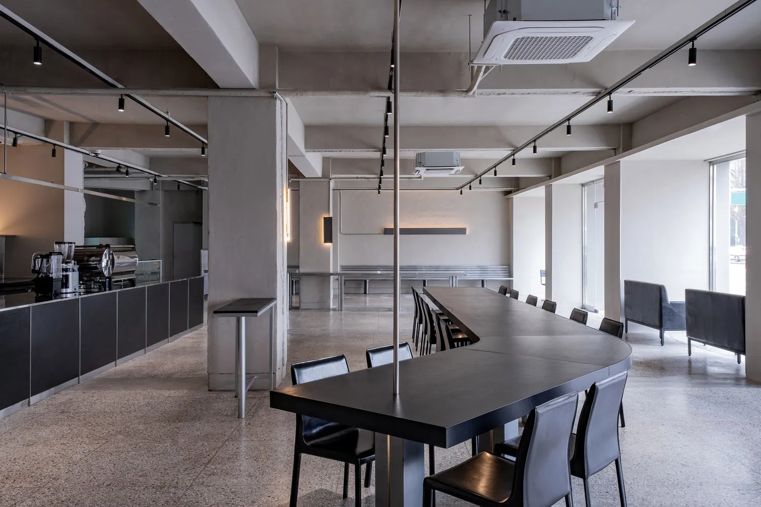 A spacious, modern cafe with a sleek concrete floor, high counter, and long dining table.
