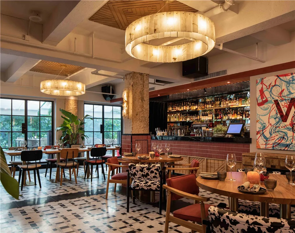 Modern restaurant interior with wooden tables and chairs, large pendant lights, and a well-stocked bar.