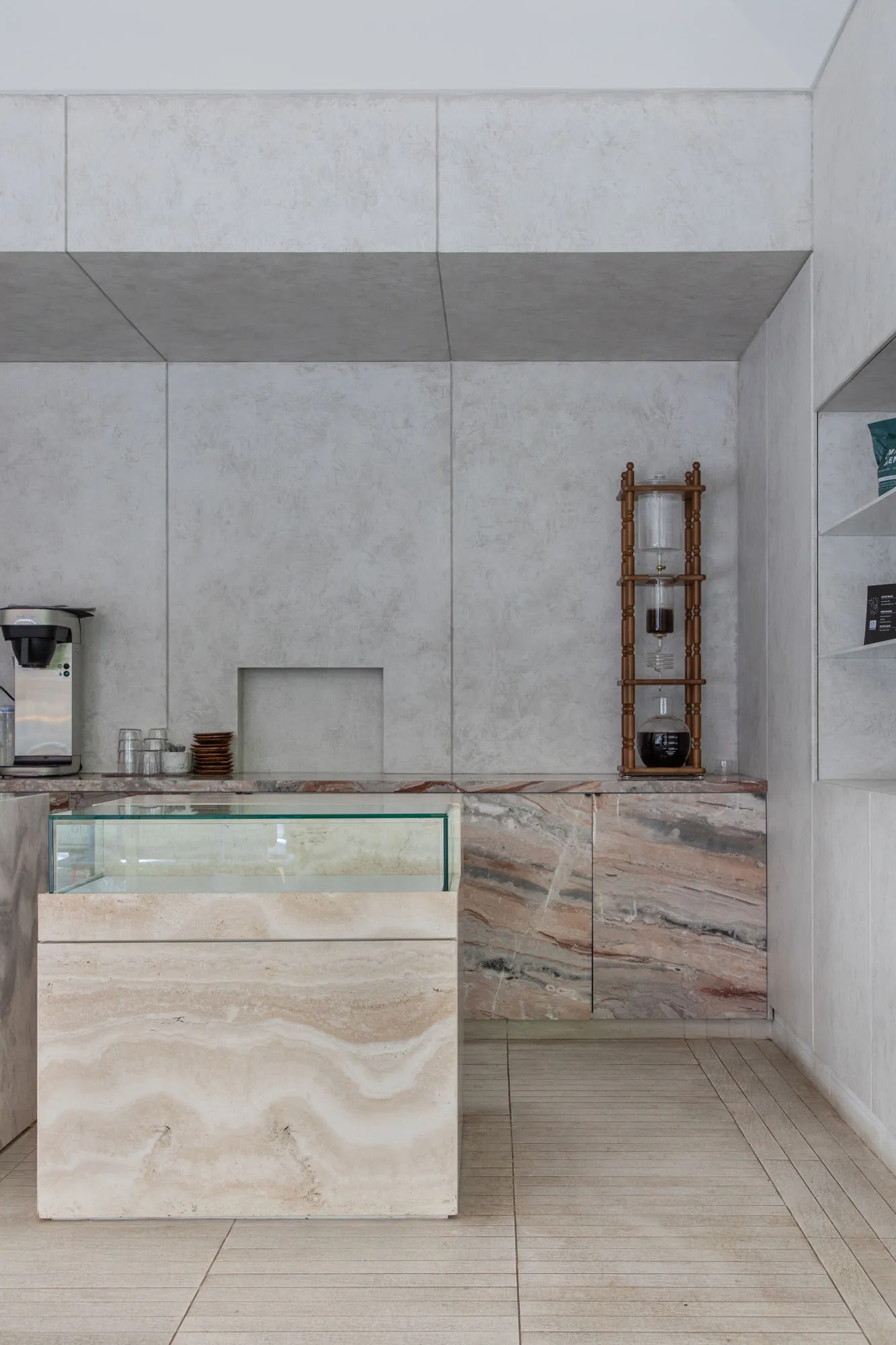 A minimalist coffee shop featuring a marble countertop with a coffee machine and a cold-brew coffee stand.