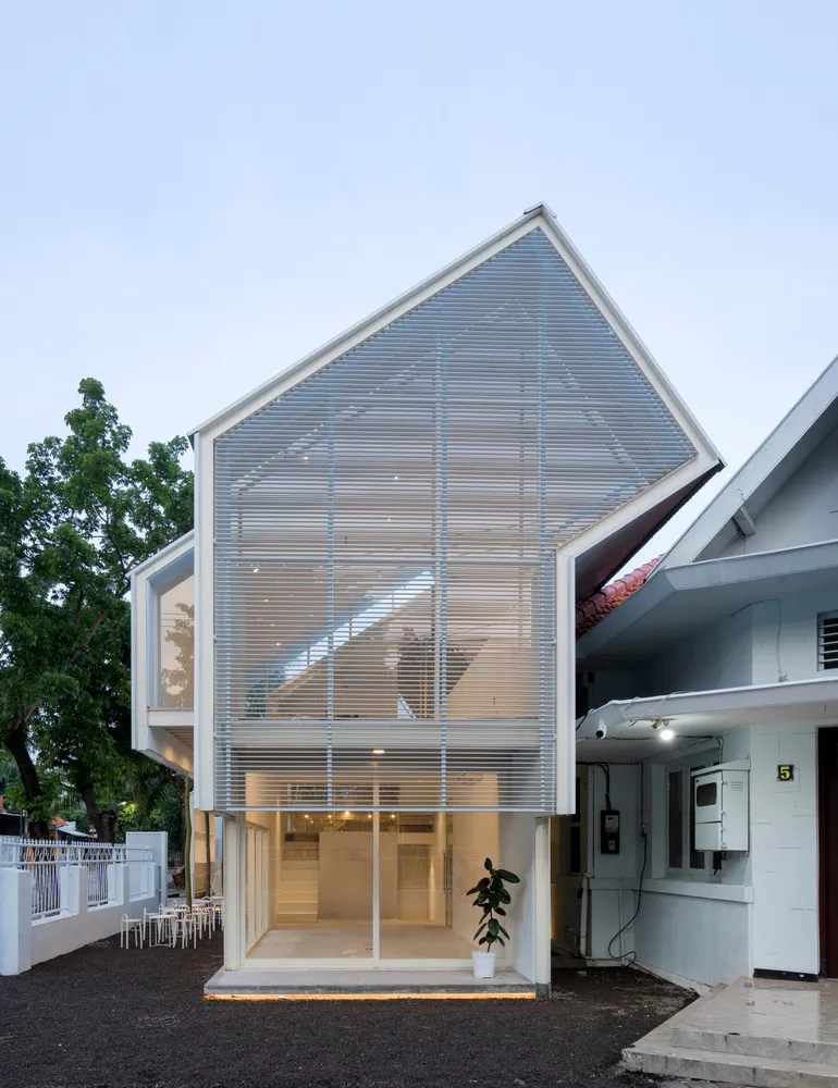 A modern house exterior with a glass wall and roof, featuring a small plant and outdoor seating area.