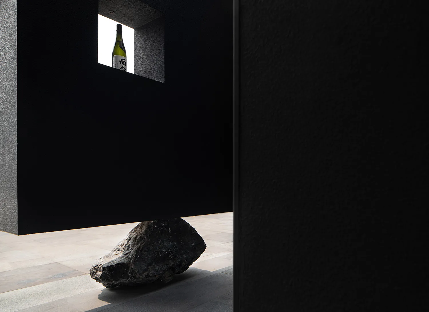 A minimalist still life featuring a stone window with a酒瓶 visible through it, set against a black background.