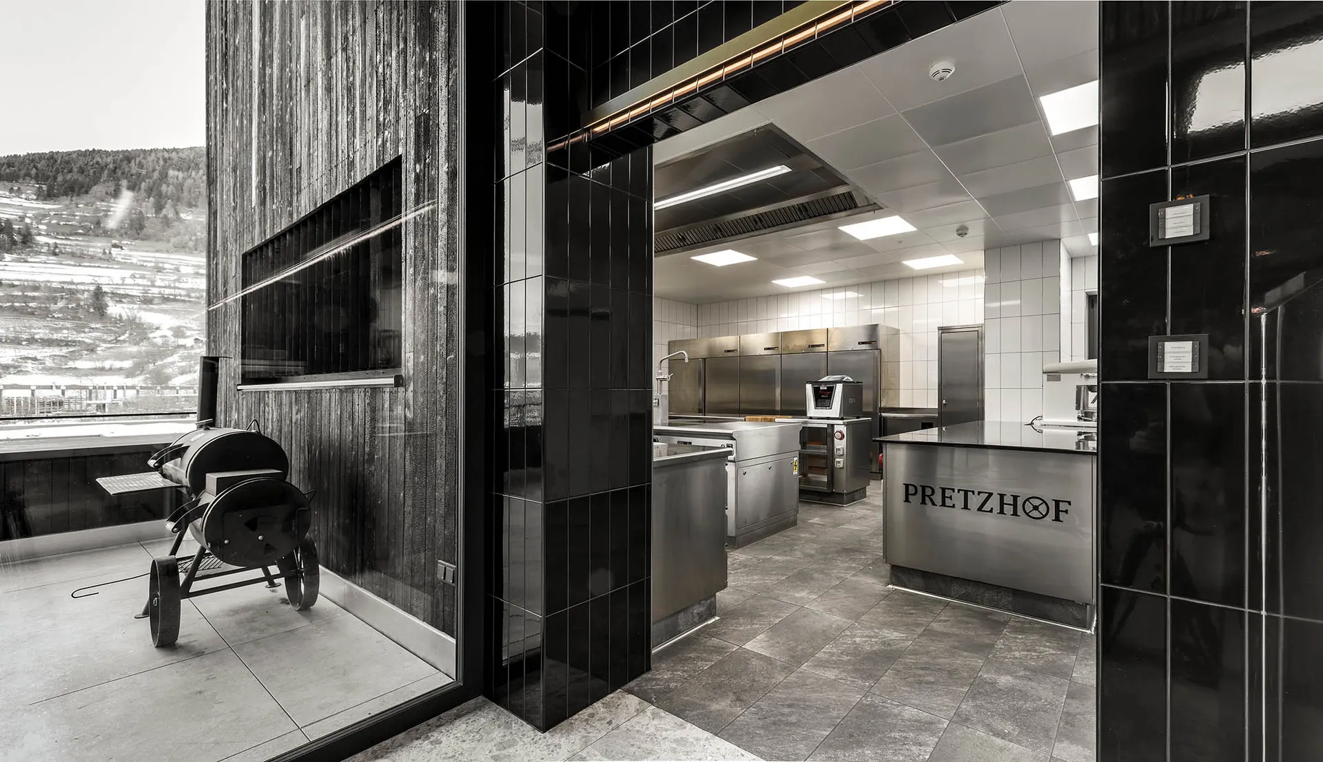 Modern commercial kitchen with stainless steel appliances and black and white tile flooring.