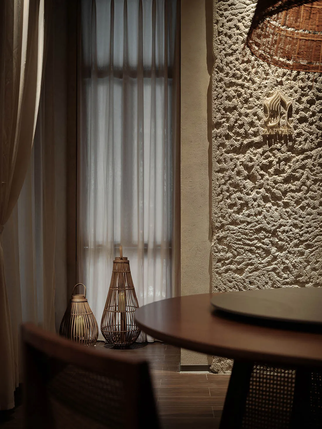 A modern restaurant interior featuring wooden textures, modern lighting, and a textured stone wall with a logo sign.