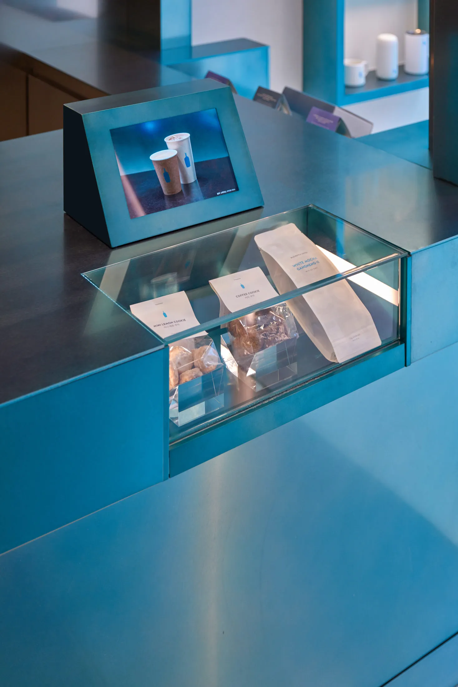 A display counter with a glass shelf showcasing coffee-related products and bags.