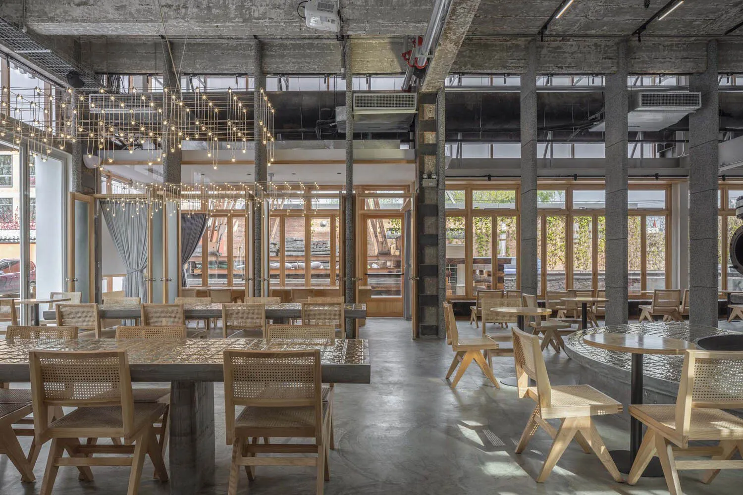 工業風餐廳室內,擺放木製桌椅,搭配混凝土地板與玻璃窗。