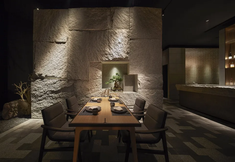 A modern dining room with a stone wall and table set for dinner.