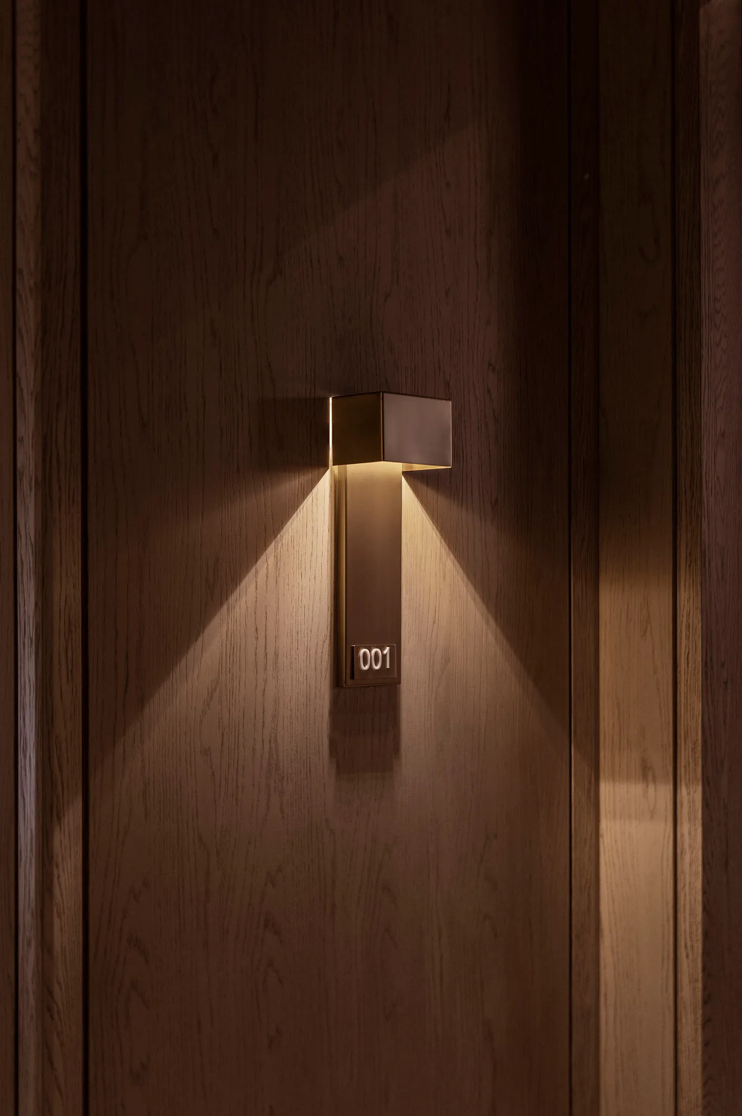 Modern metallic brass number plate wall light with light shining upwards.