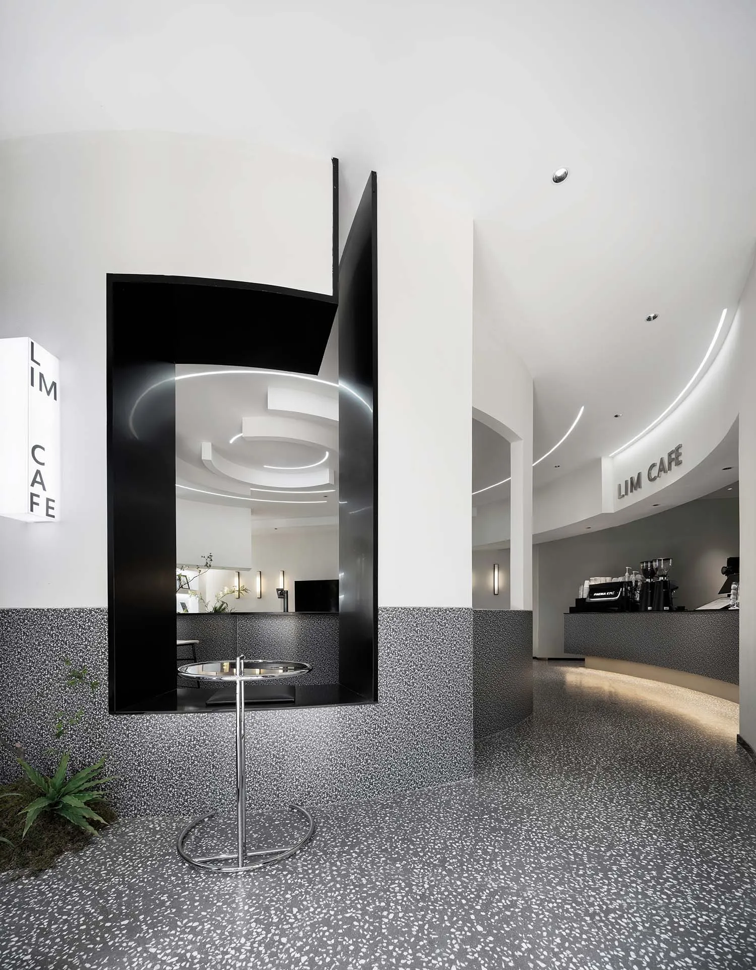 Modern cafe interior with black geometric walls, terrazzo flooring, and concrete columns