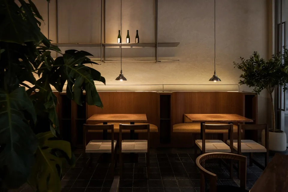 A minimalist restaurant interior with wooden tables, fabric chairs, and concrete accents.