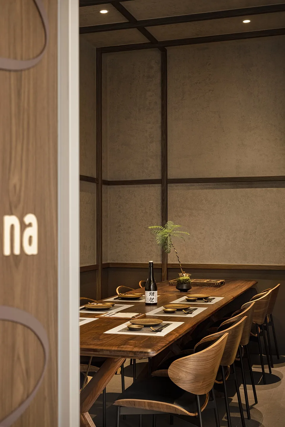 Modern restaurant interior with wooden tables, chairs, and a bottle of sake.