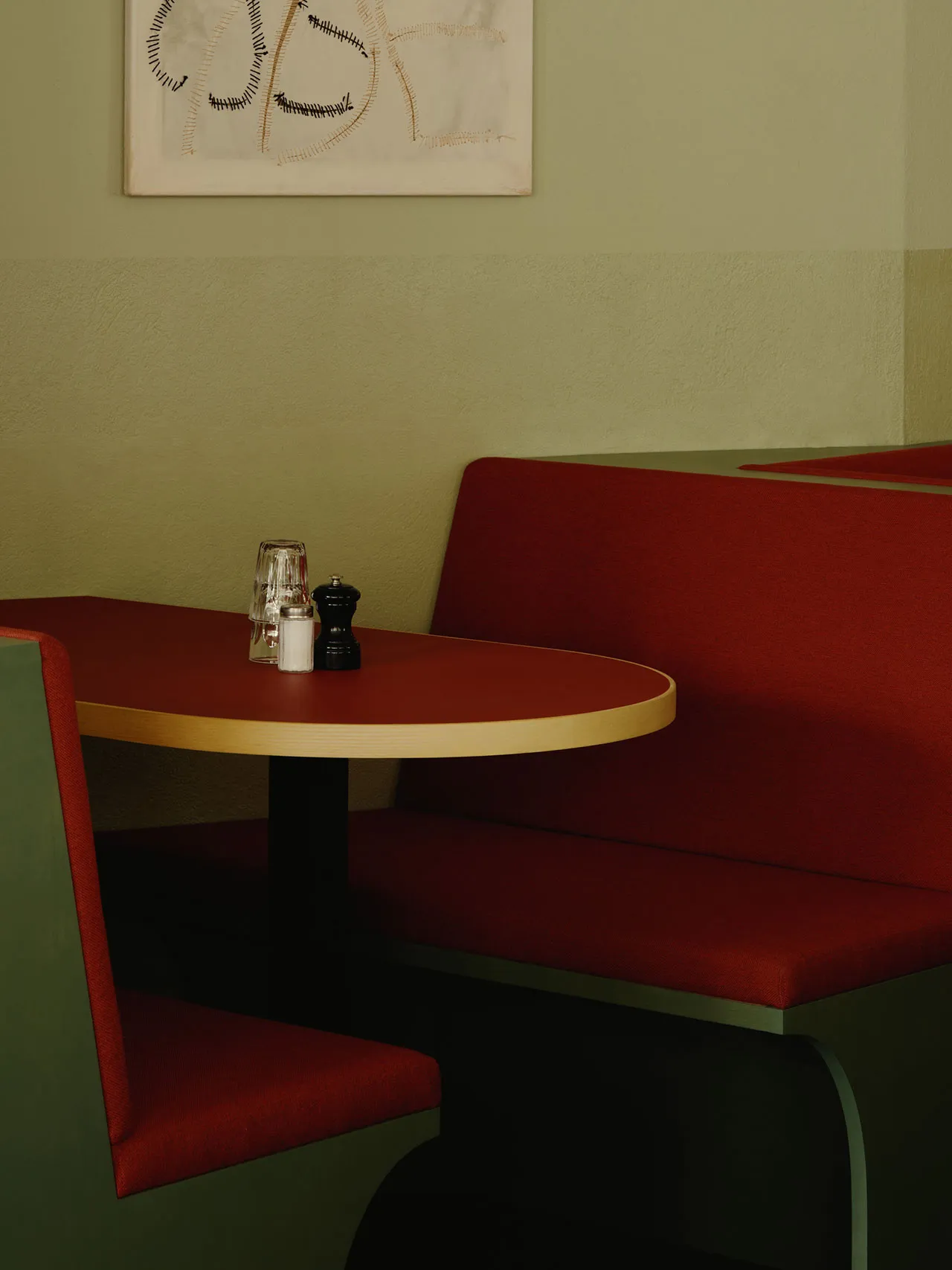 A booth camera in a restaurant interior featuring a red upholstered bench with a white wall in the background.