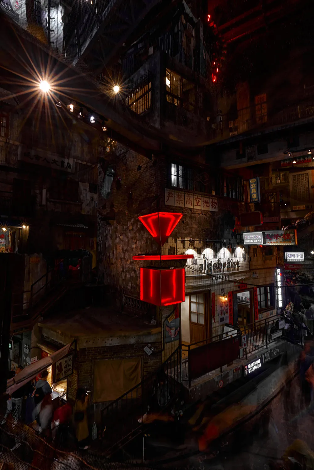 Urban night scene featuring a large red spinner suspended from a building, surrounded by illuminated signs and lights.