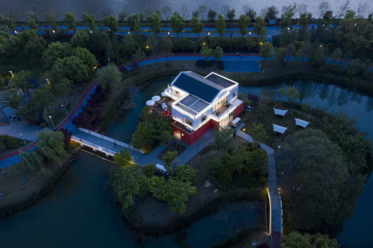 A modern house surrounded by trees and illuminated by nightlights in a park setting.