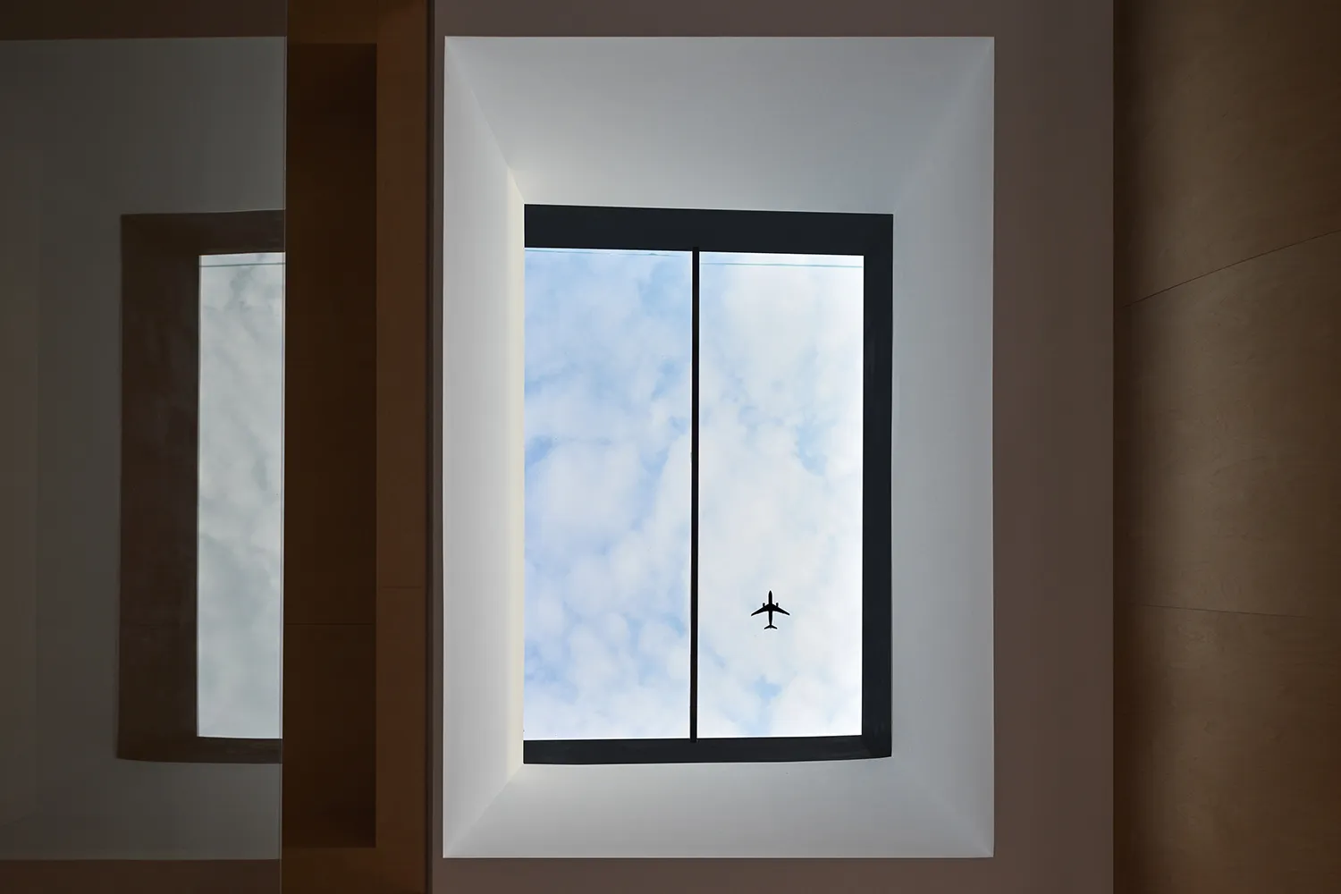 A window view with an airplane flying in the blue sky.