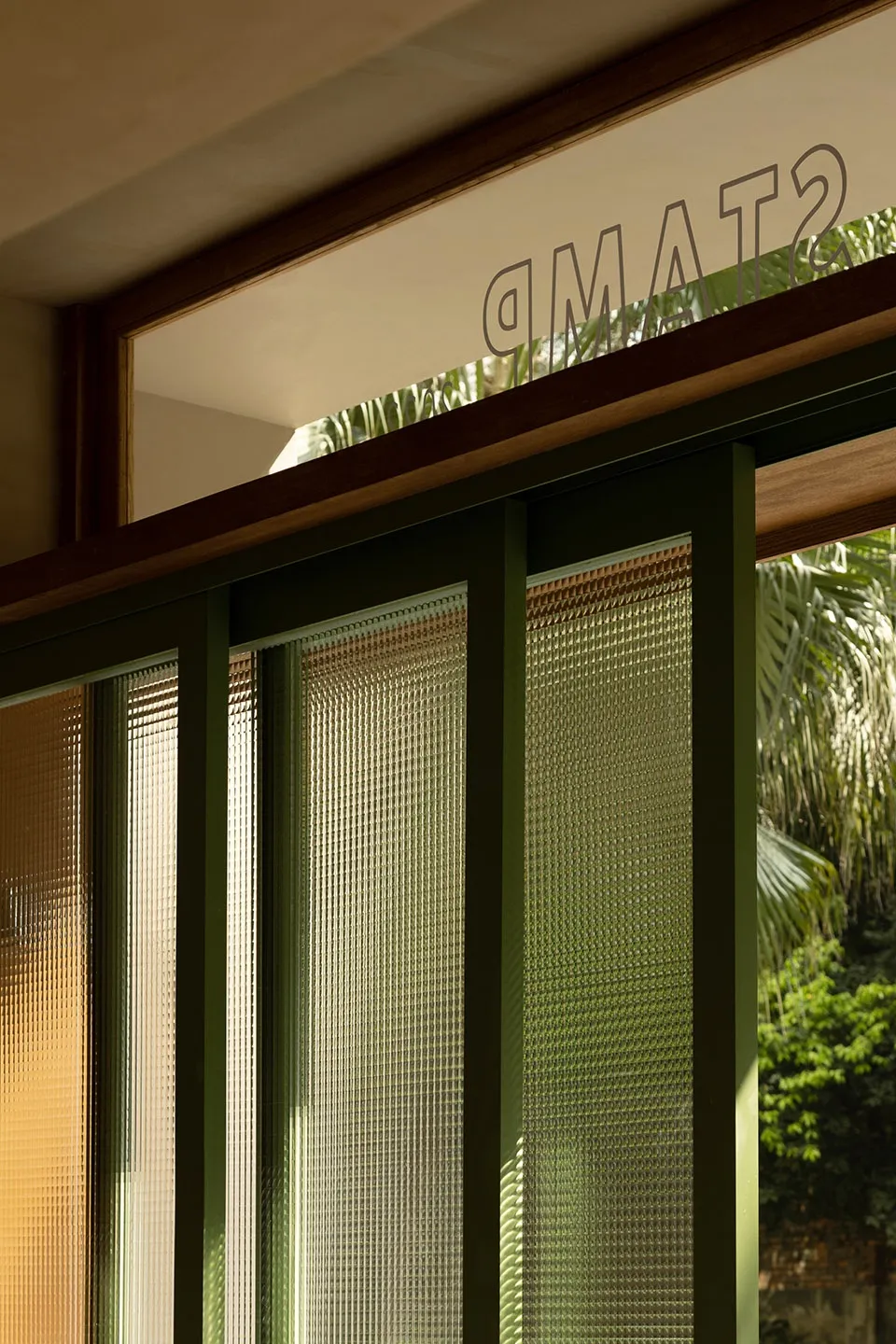 A modern glass door with a textured pattern, seen from the inside looking out towards a tropical garden.