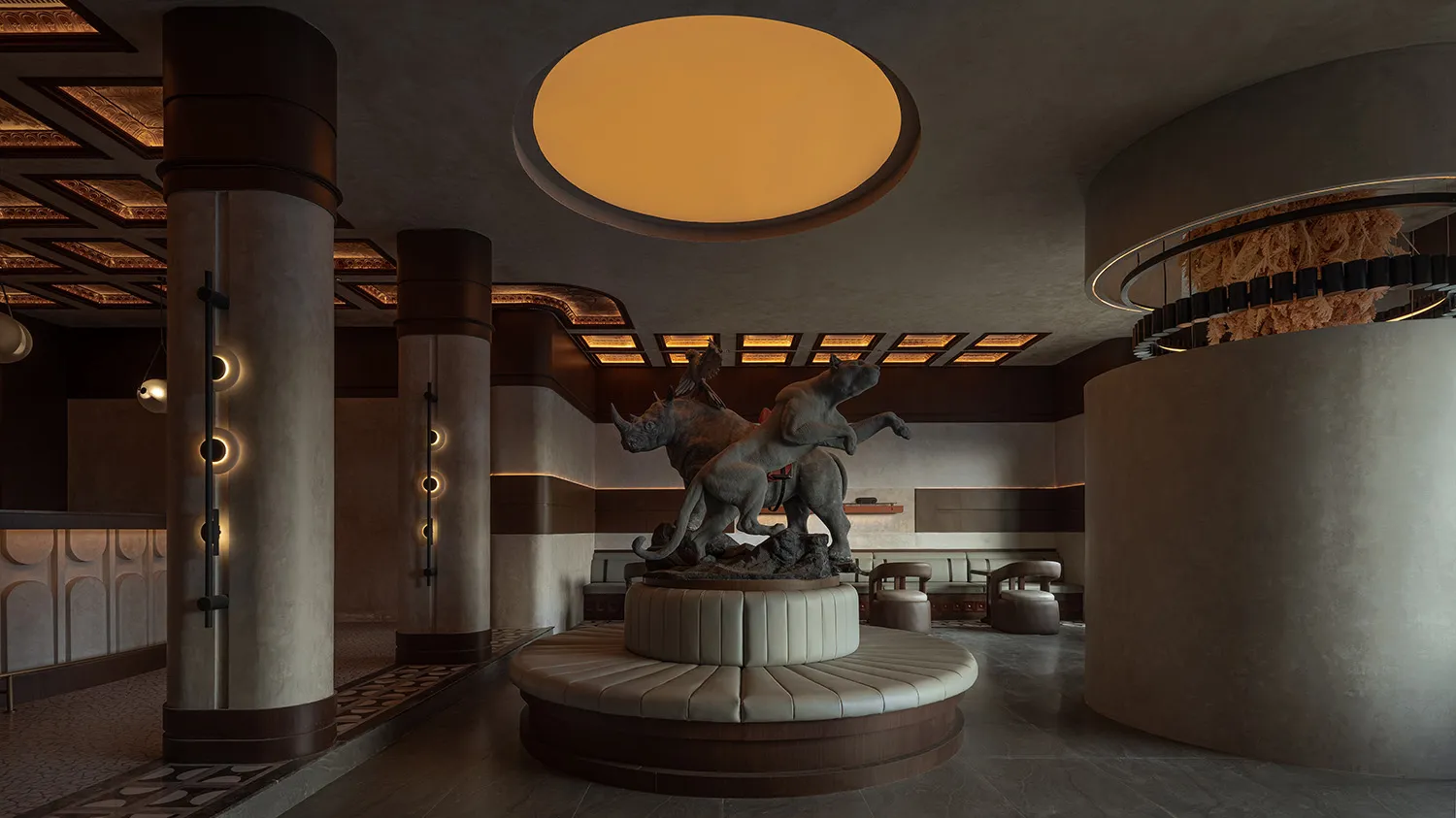 A modern hotel lobby with concrete columns, a circular light fixture, and a statue of a lion and a rhinoceros.