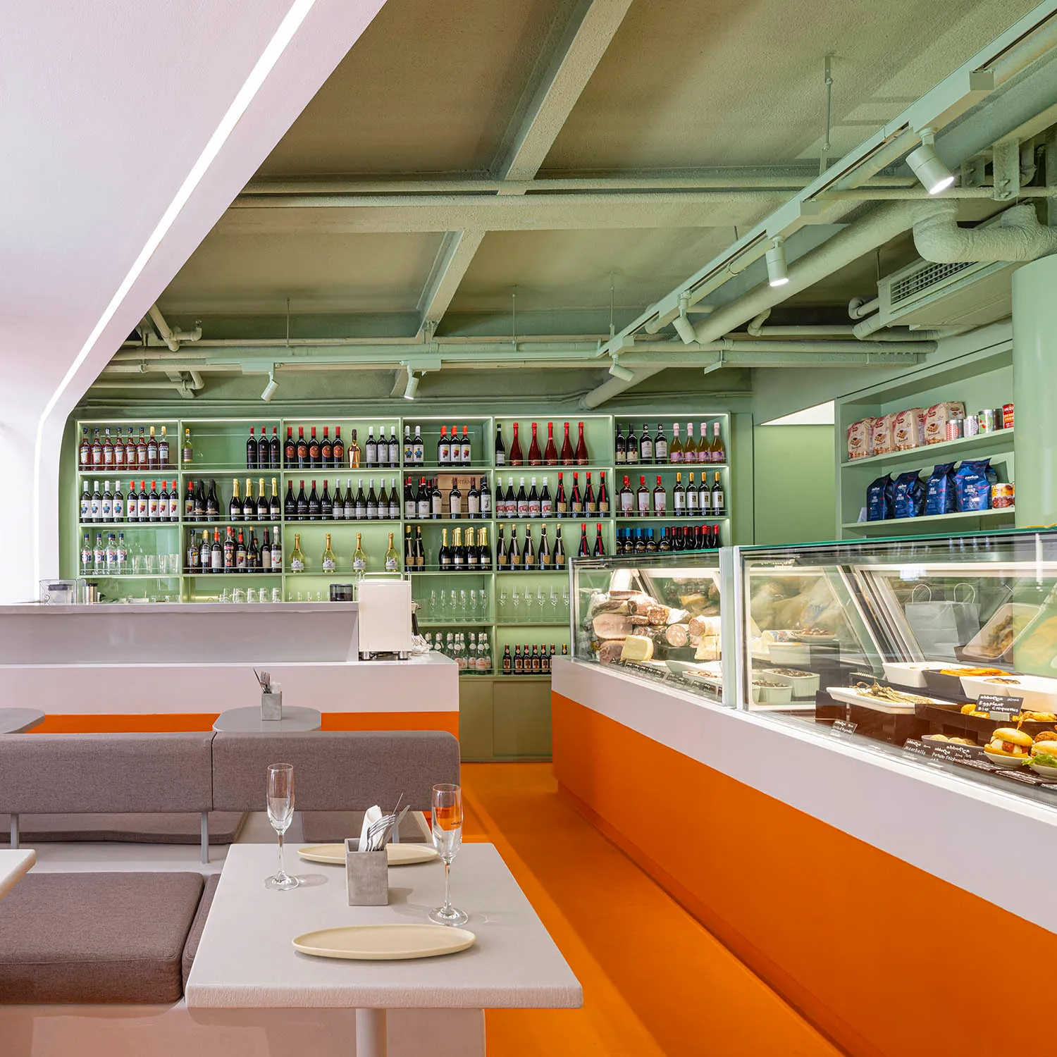 A modern restaurant interior with orange shelves displaying wine bottles, concrete ceiling, and glass shelves.
