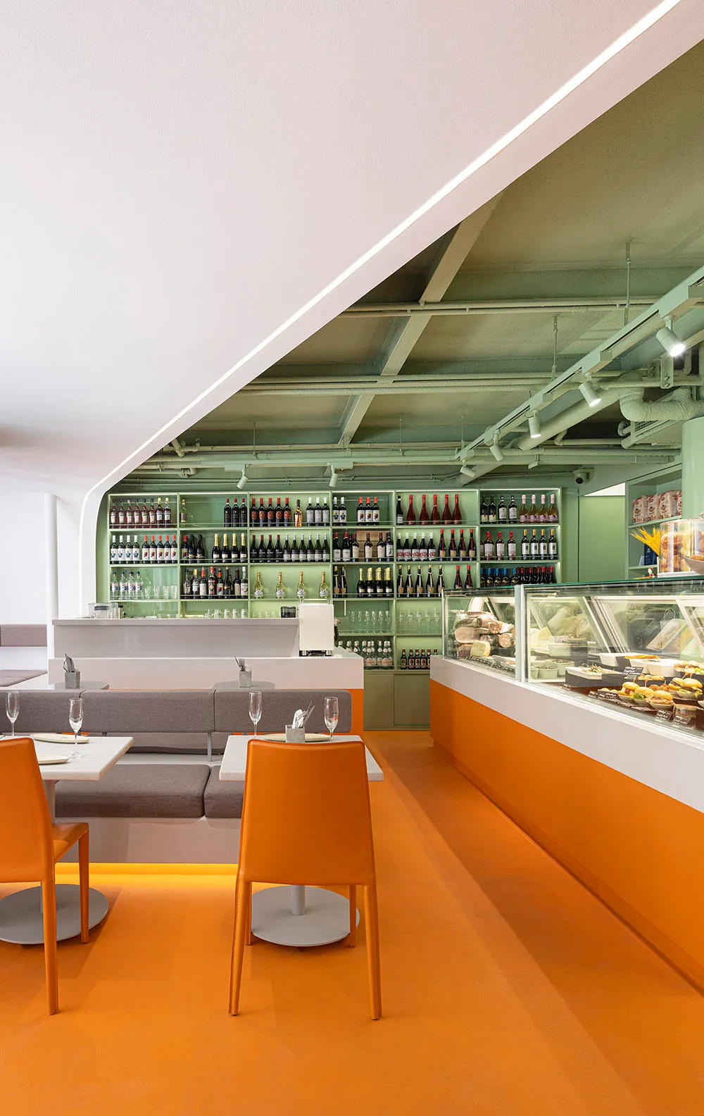Modern restaurant interior with orange floor, white walls, concrete counter, and green shelving.