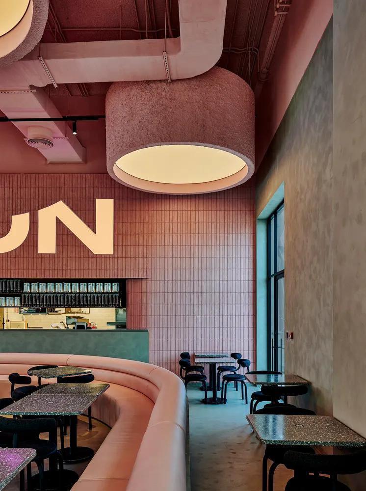 A modern cafe interior with pink tiles on the walls, concrete flooring, and circular pendant lights.