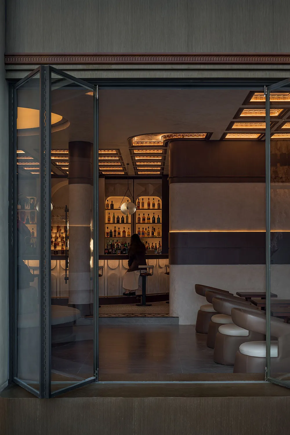 Modern bar interior with neutral-toned decor and illuminated shelves.
