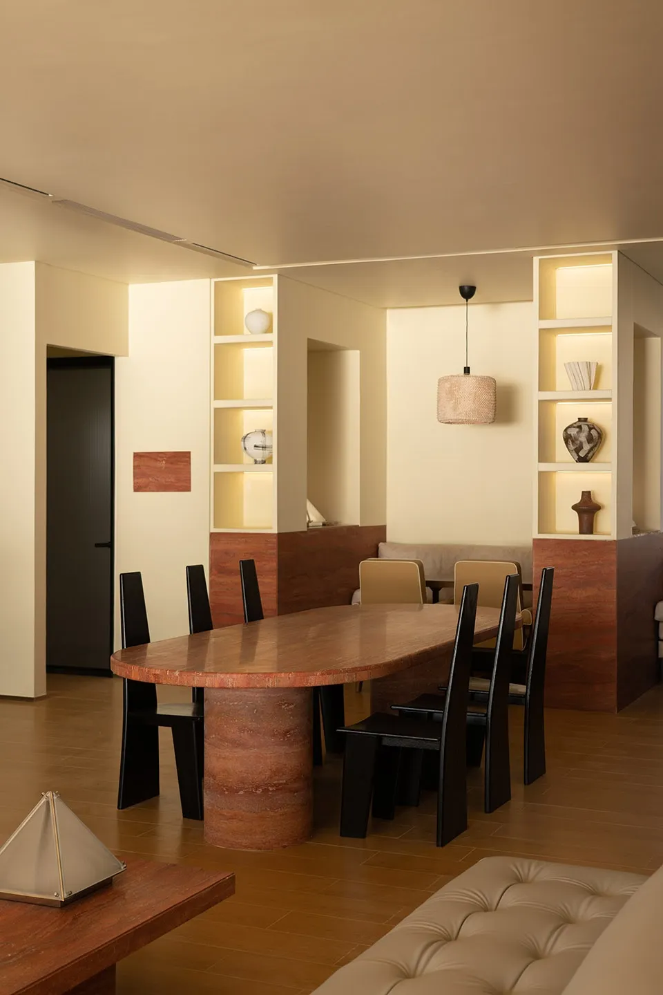 A minimalist dining room with a sandstone table and black chairs.
