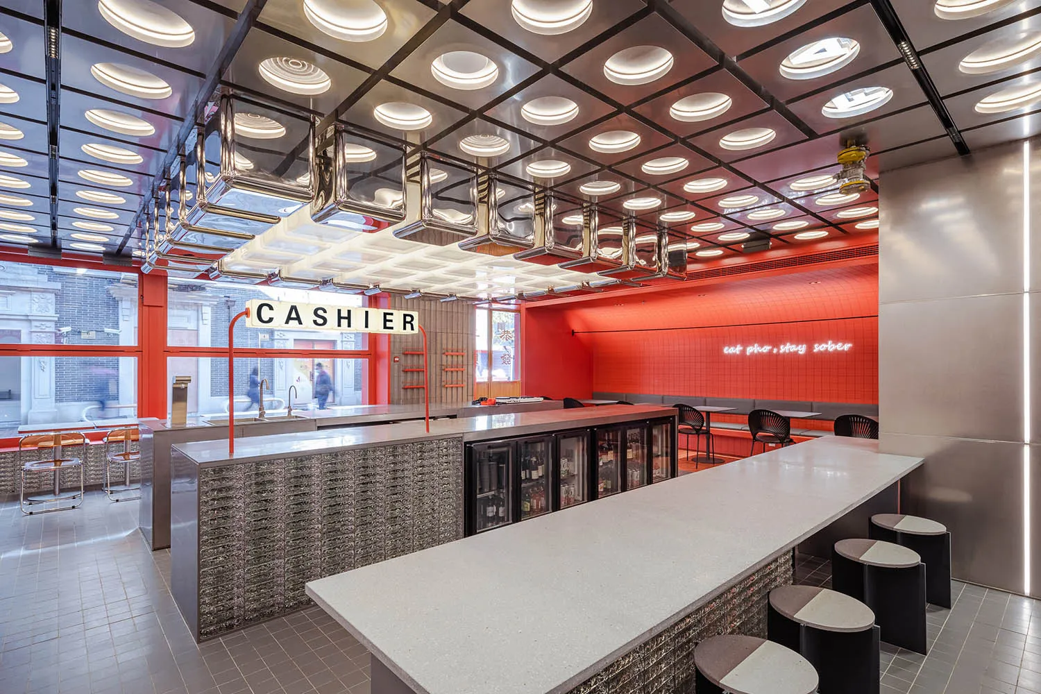 A modern cafe bar interior with metallic finishes, red tiled walls, and glass elements.