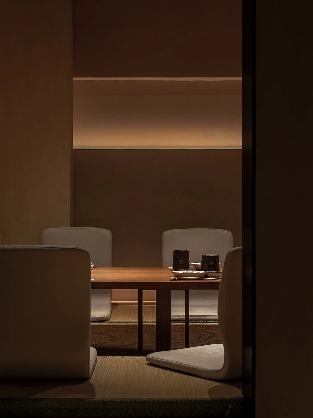 A minimalist restaurant interior with wooden furniture and warm lighting.