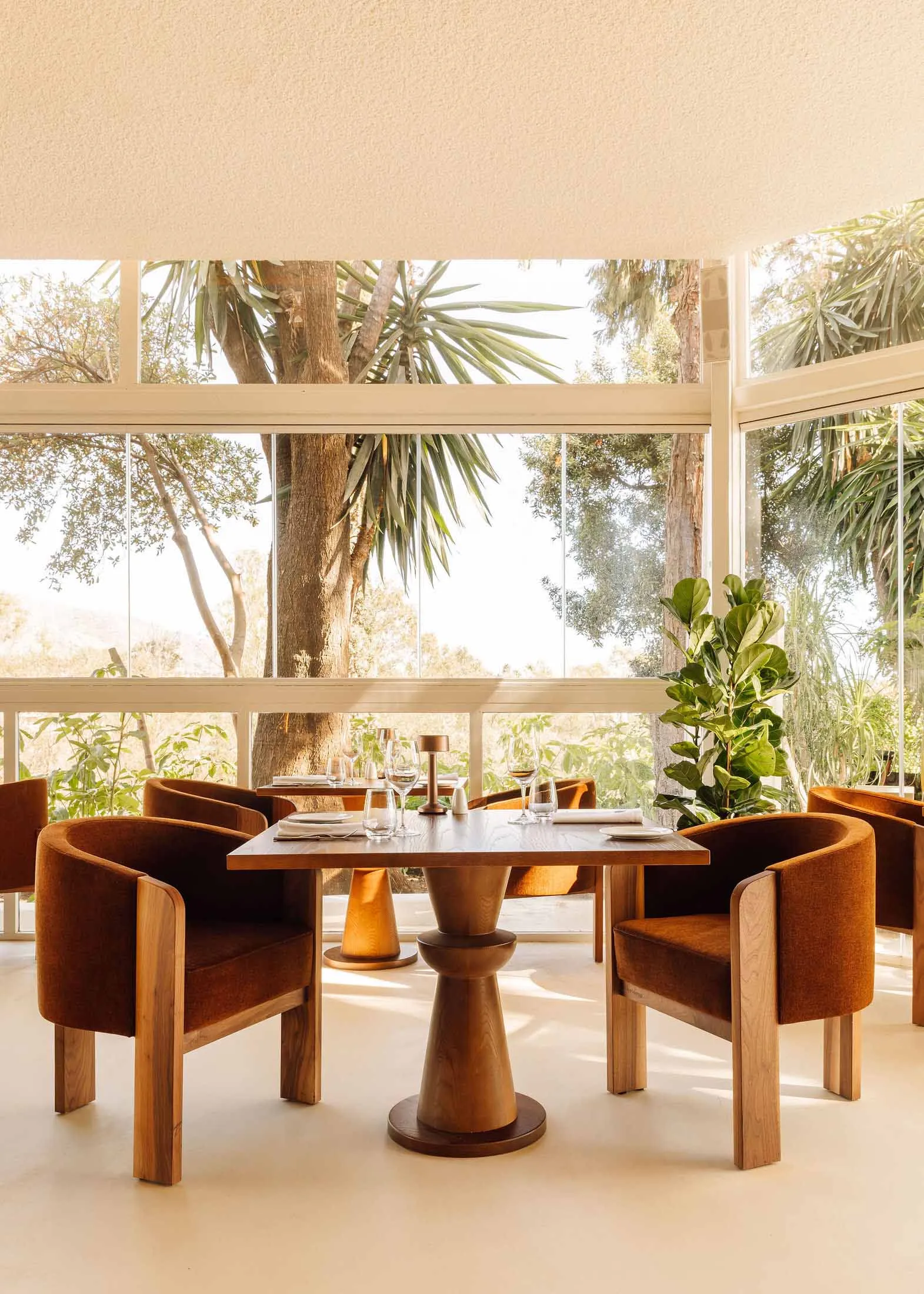 A modern restaurant interior with wooden furniture, featuring large windows and a view of the outdoors.