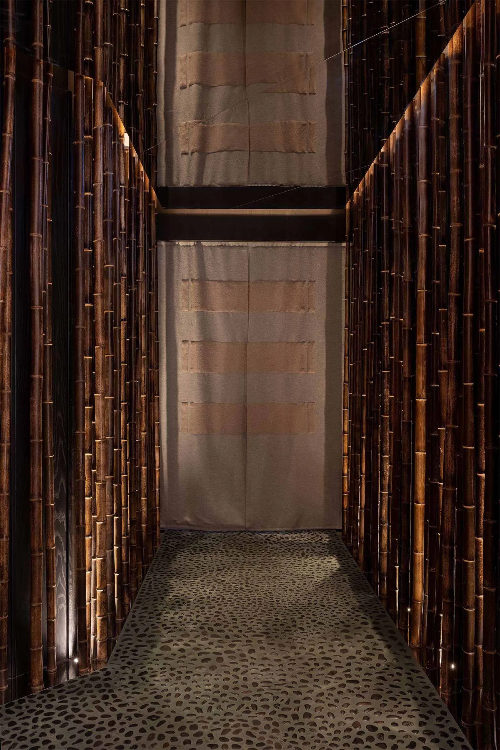 Decorative bamboo corridor with textured floor and light filtering through curtains.