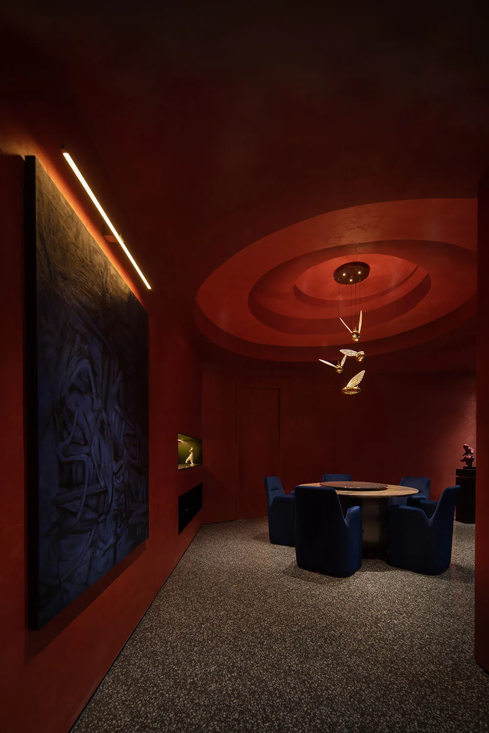 A modern dining room with metallic textures, featuring a round table, blue chairs, and a circular ceiling design.