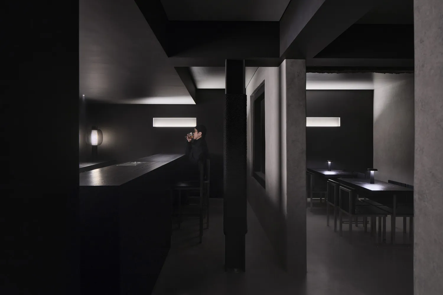 A minimalist restaurant interior with black concrete walls and lighting fixtures