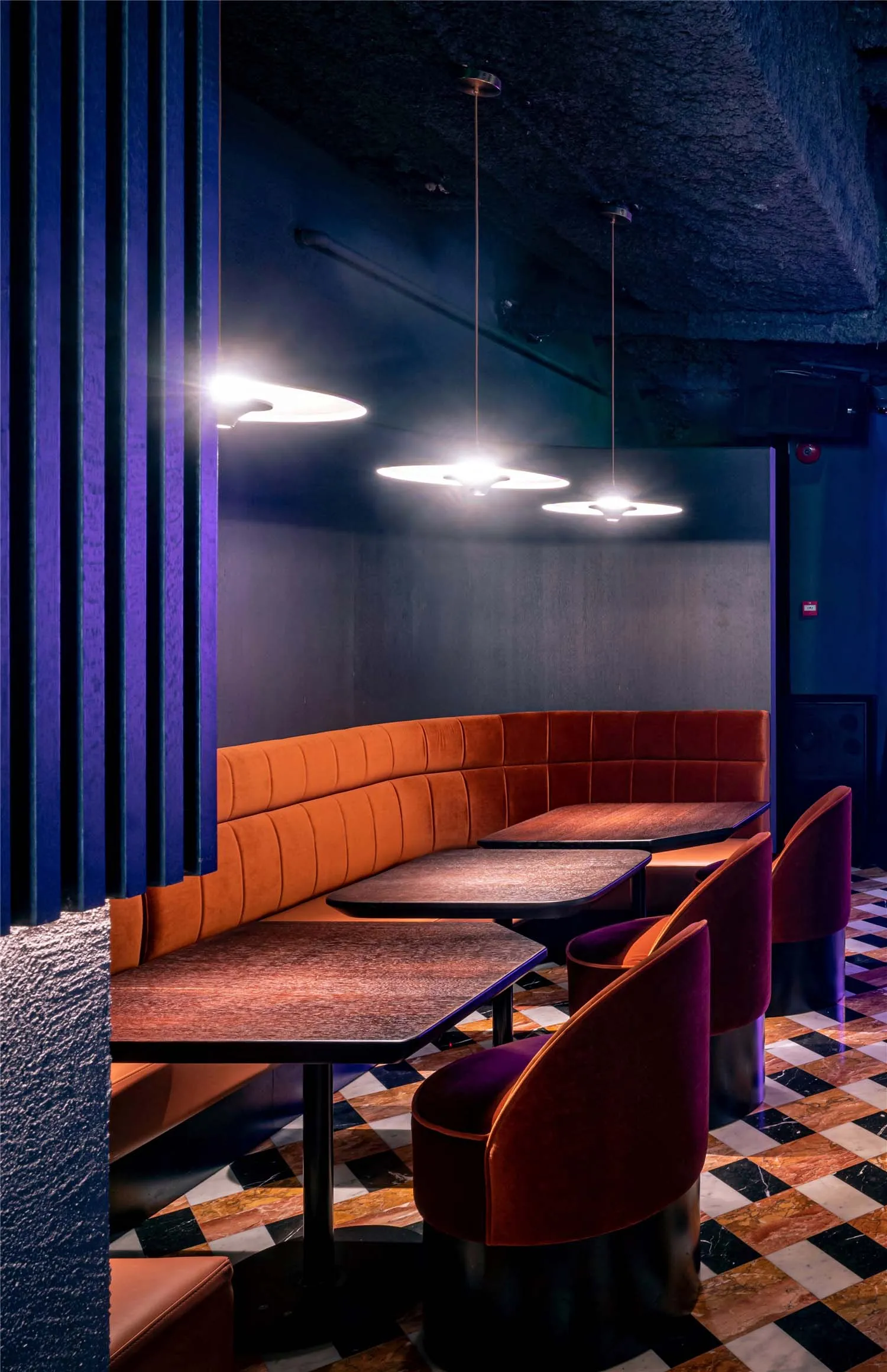 A stylish restaurant interior with velvet booth seating, wooden tables, and marble flooring.