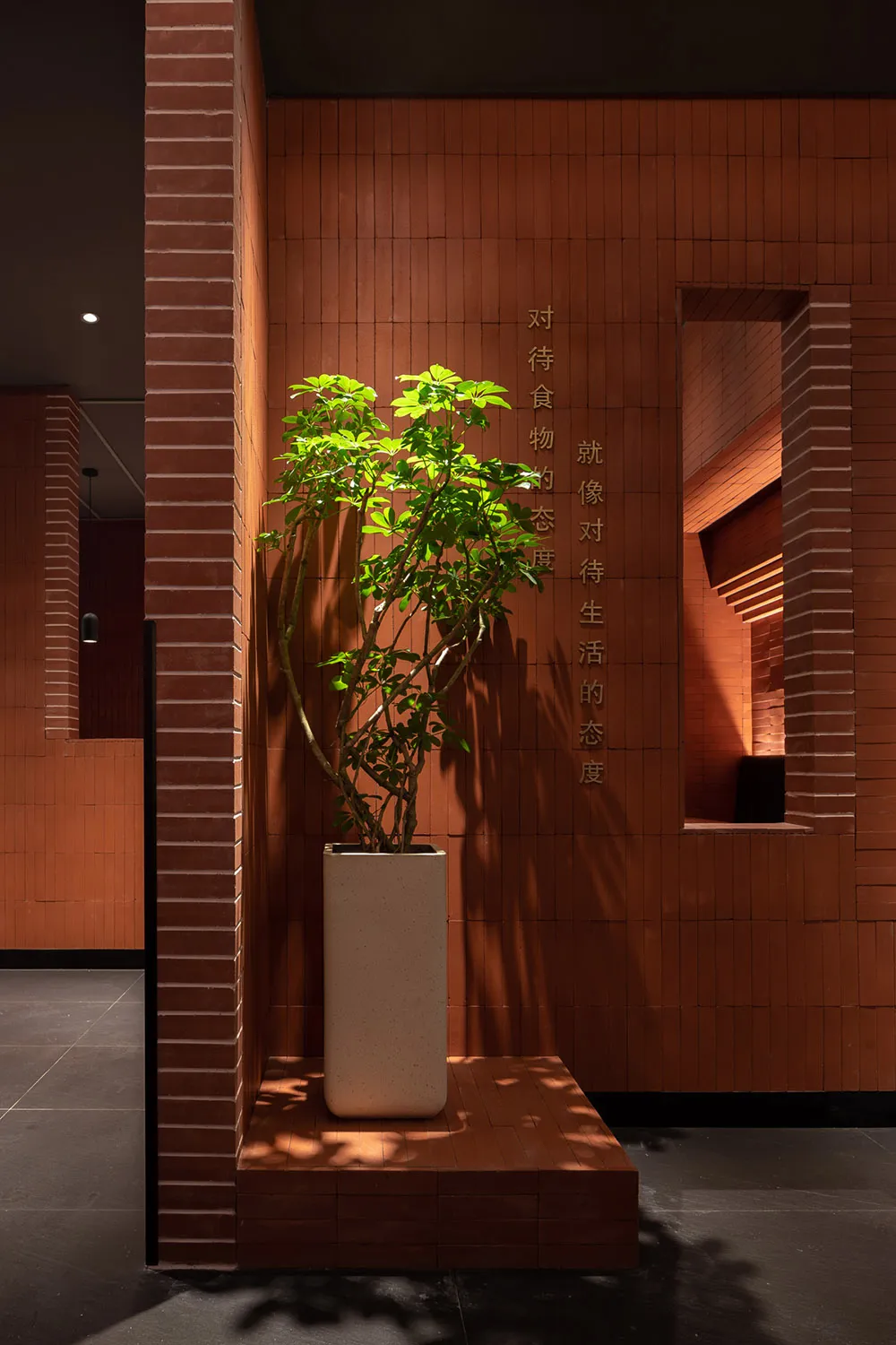 An industrial-style restaurant entryway featuring brick tiles, concrete, and a potted plant.