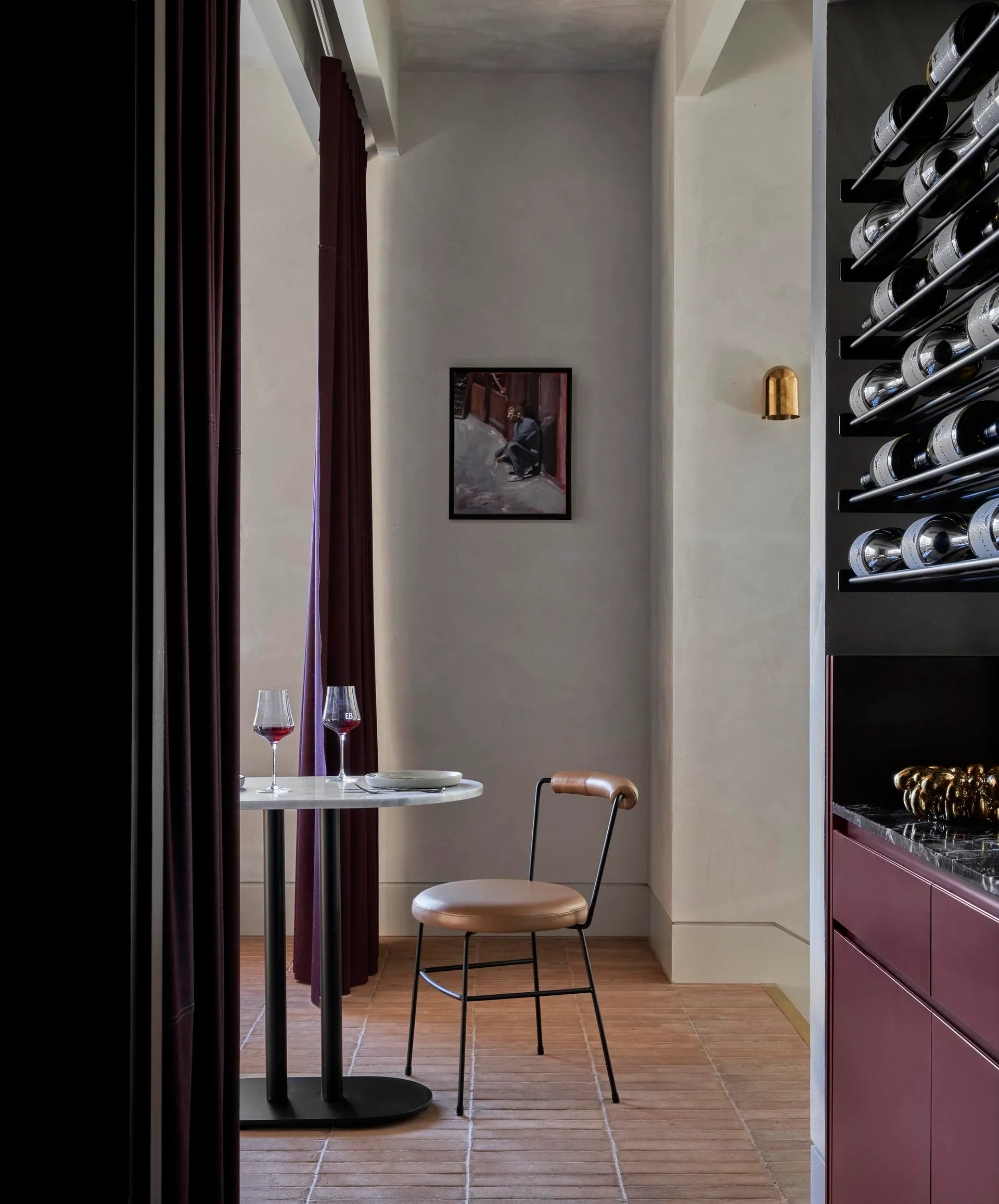 A modern wine bar with metal and leather furniture, featuring a round table with wine glasses and a chair.