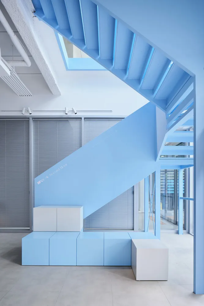 Modern minimalist office interior with a blue steel staircase and white concrete elements