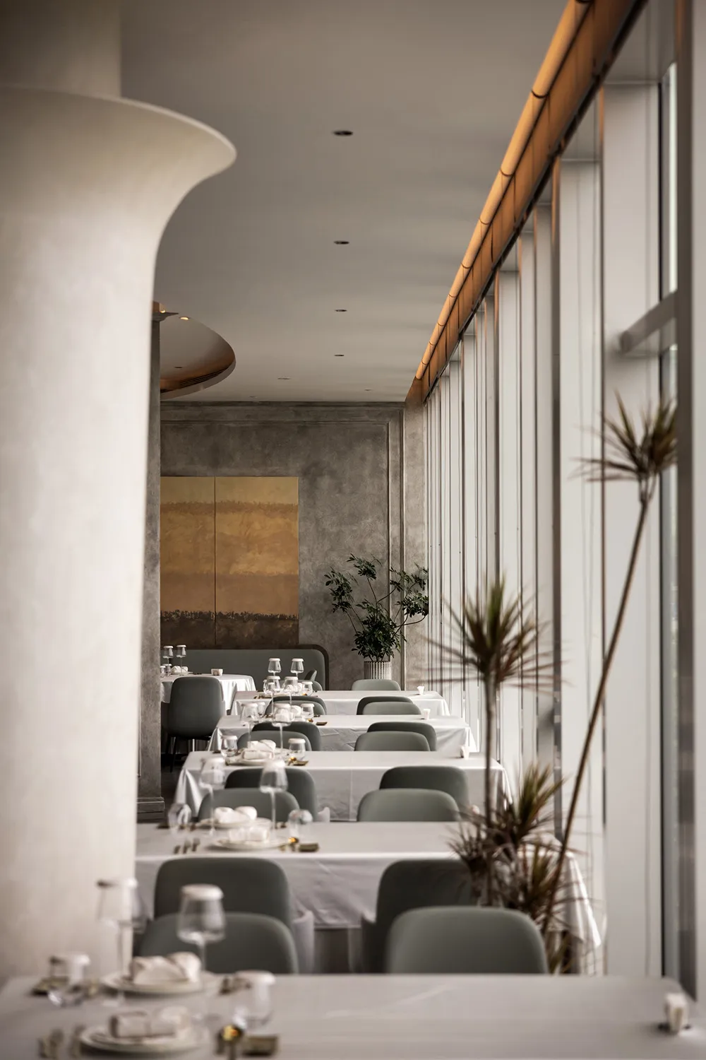 A minimalist restaurant interior with white walls, concrete columns, and large windows.