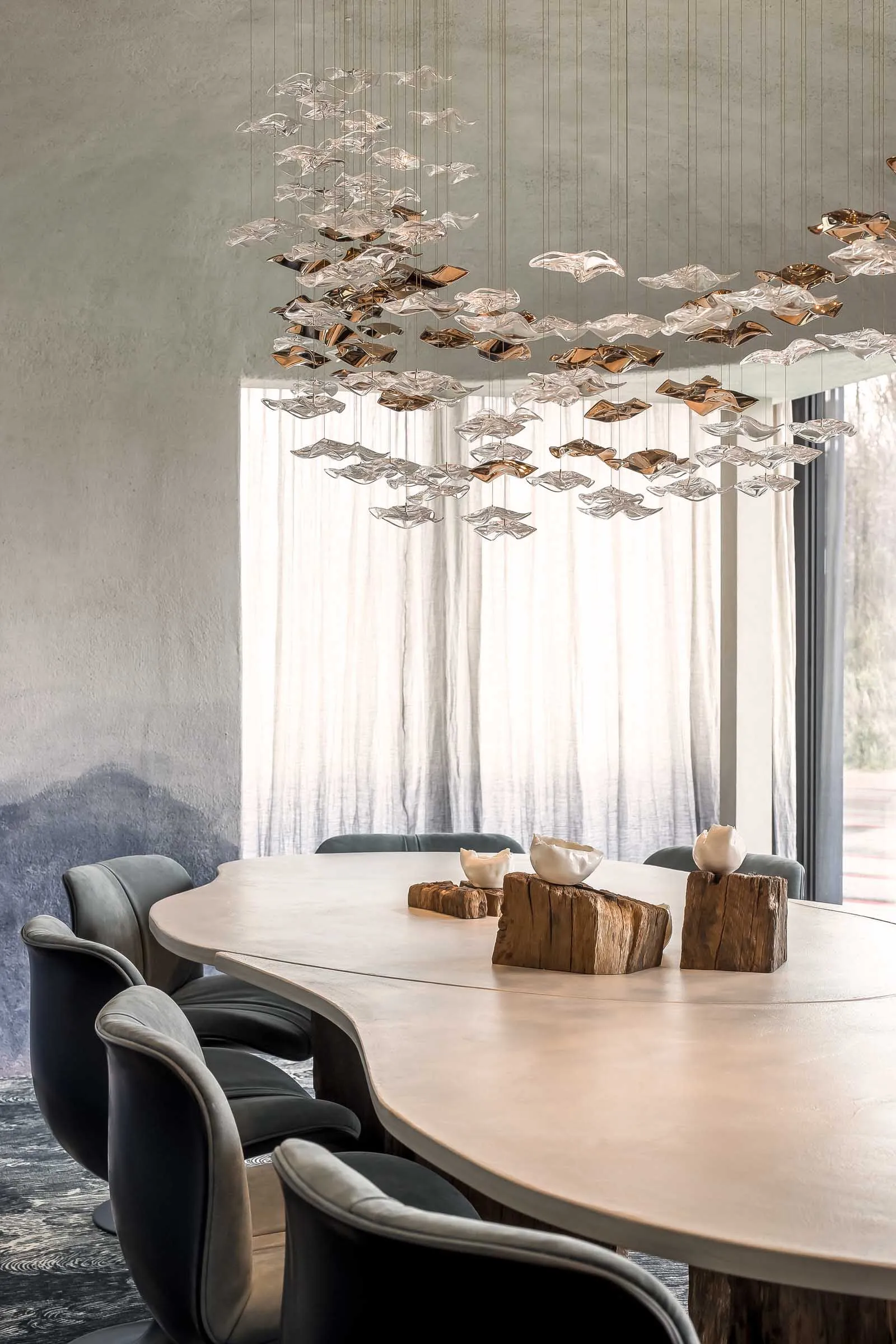 Modern dining room featuring a large table with wooden texture and hanging glass light fixture resembling flowing leaves.