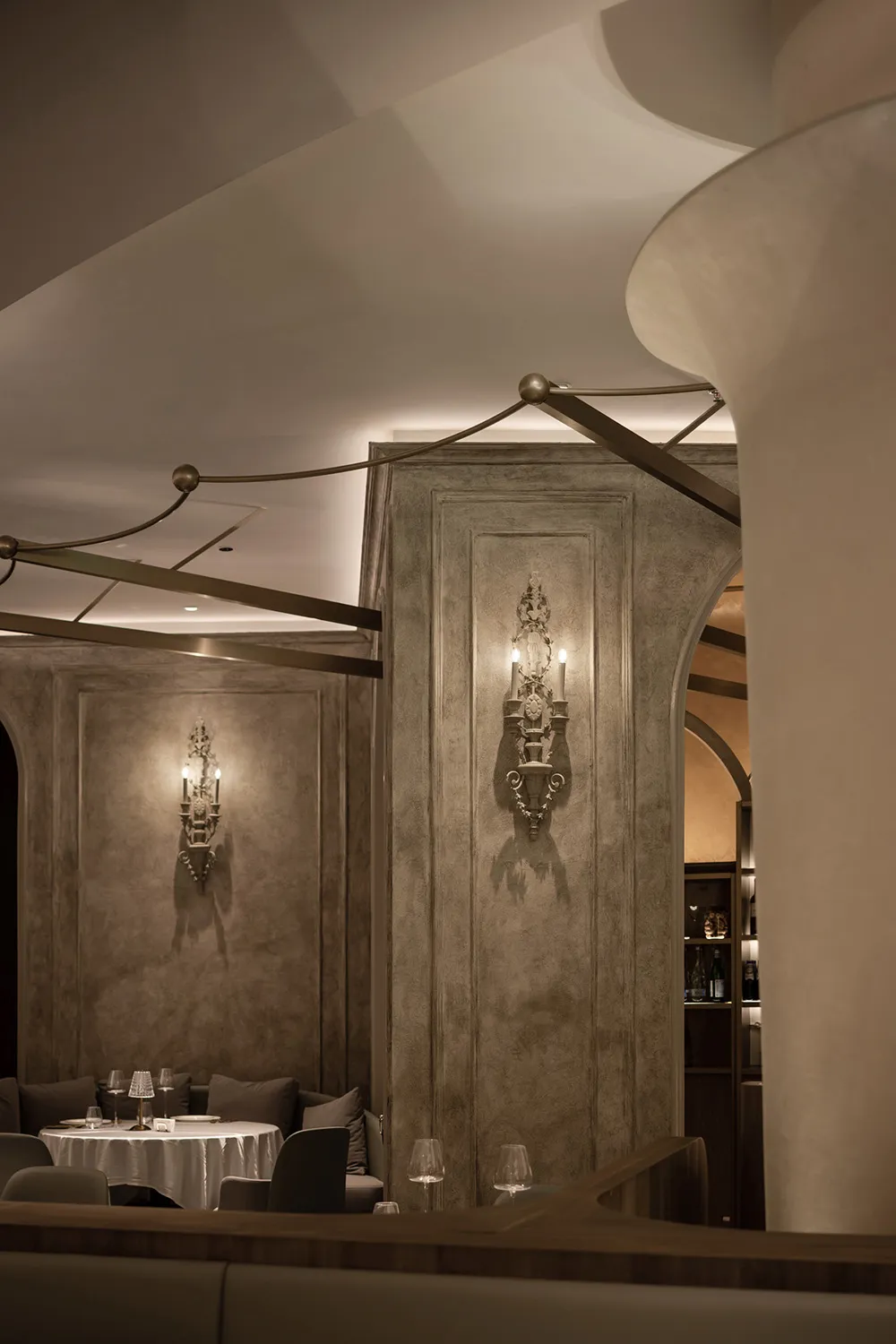 A modern restaurant with a concrete floor and stone walls, featuring elegant sconce lighting.