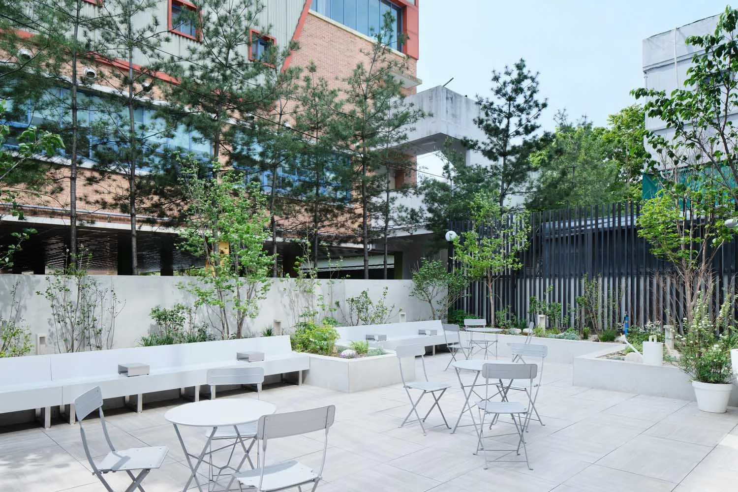 Concrete outdoor seating area with white furniture, greenery, and garden tiles.