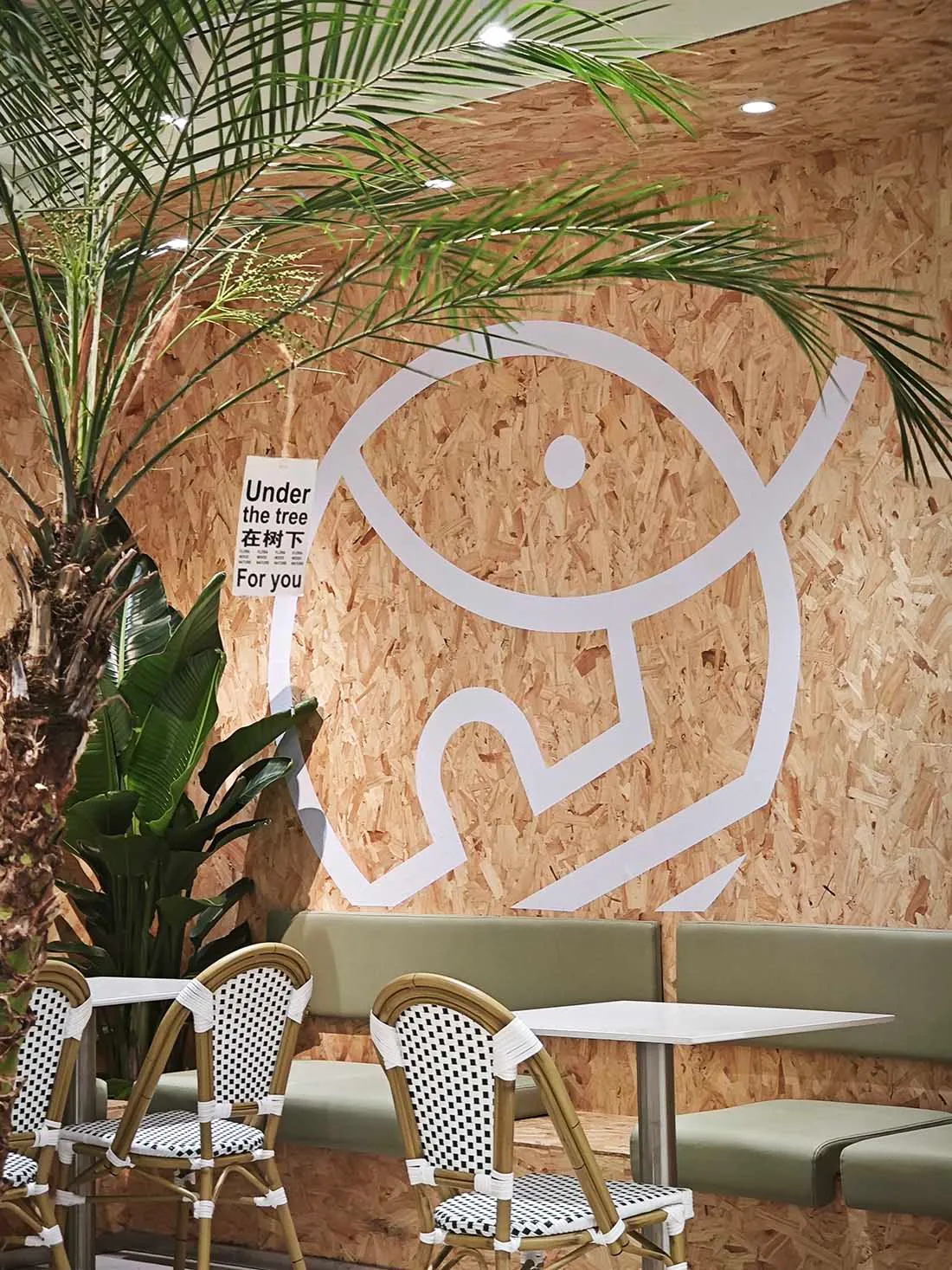 A café interior featuring natural materials, with a sign that says 'Under the tree' and a large tree plant.