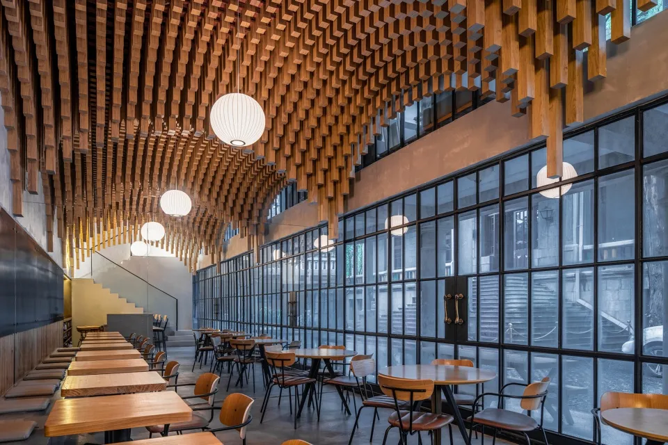 Contemporary wooden restaurant interior with hanging lamps and large windows.
