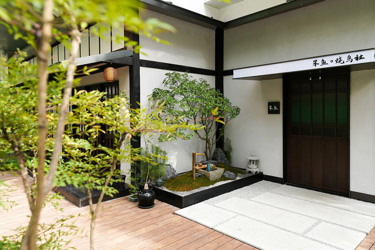 A serene minimalist entrance yard with wooden walkway, grass, and stone elements.