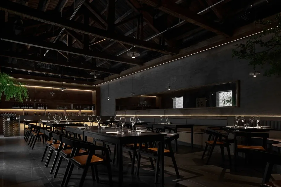 A dark, industrial-style restaurant with black steel chairs, concrete flooring, and wooden elements.