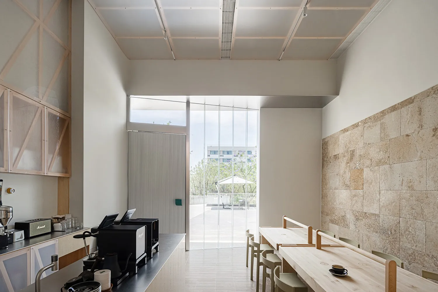 Modern minimalist cafe interior featuring wooden tables and chairs, glass dividers, and white walls and ceiling.