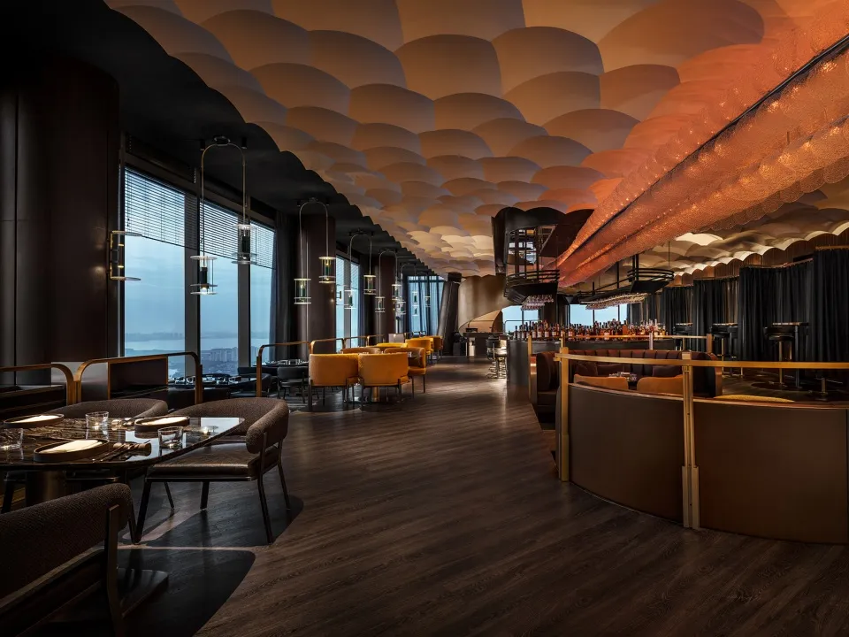 Modern restaurant interior with wood floors, metal railings, glass walls, and fabric seating.