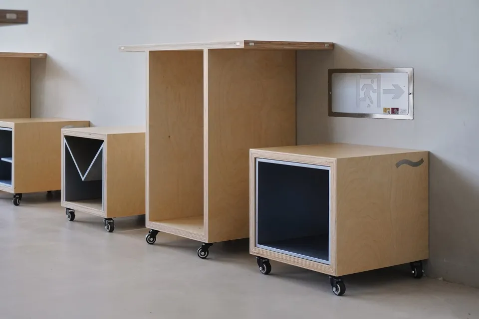 A row of minimalist storage units and cabinets with painted wood in front of an emergency exit sign.