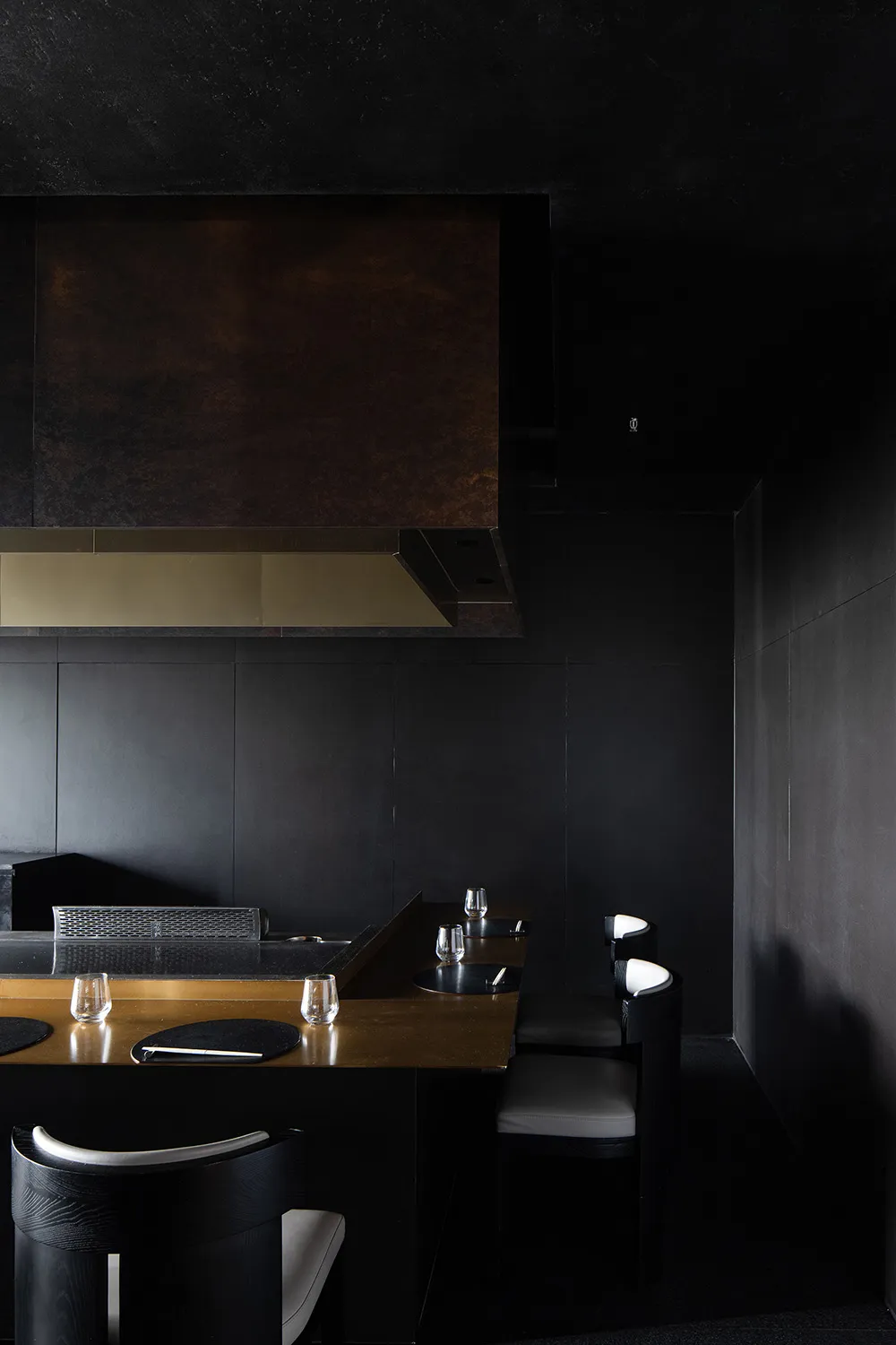 A minimalist design featuring black leather chairs, black metal table, and a black wall with a golden counter.