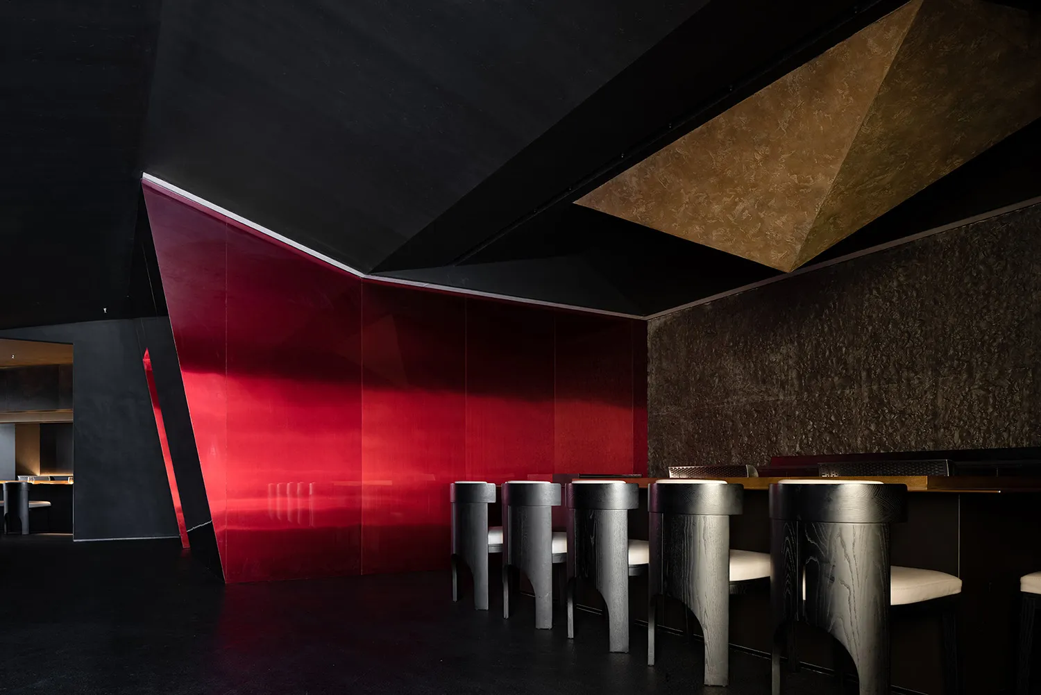 A sleek, modern restaurant interior featuring a glass bar counter with a geometric ceiling design.