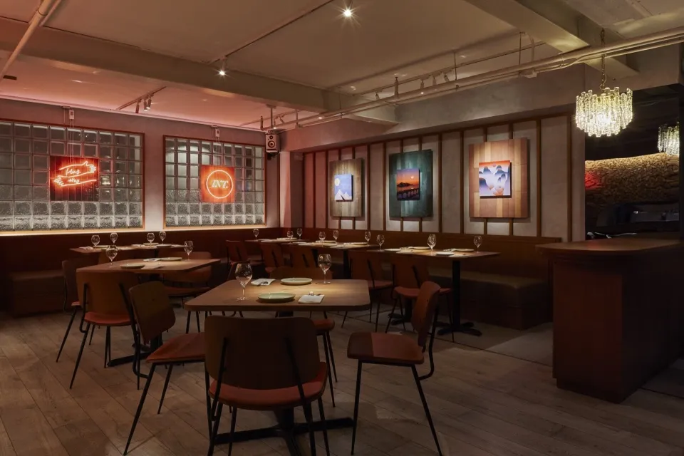 Modern restaurant interior with wooden tables, tiled benches, and contemporary art.
